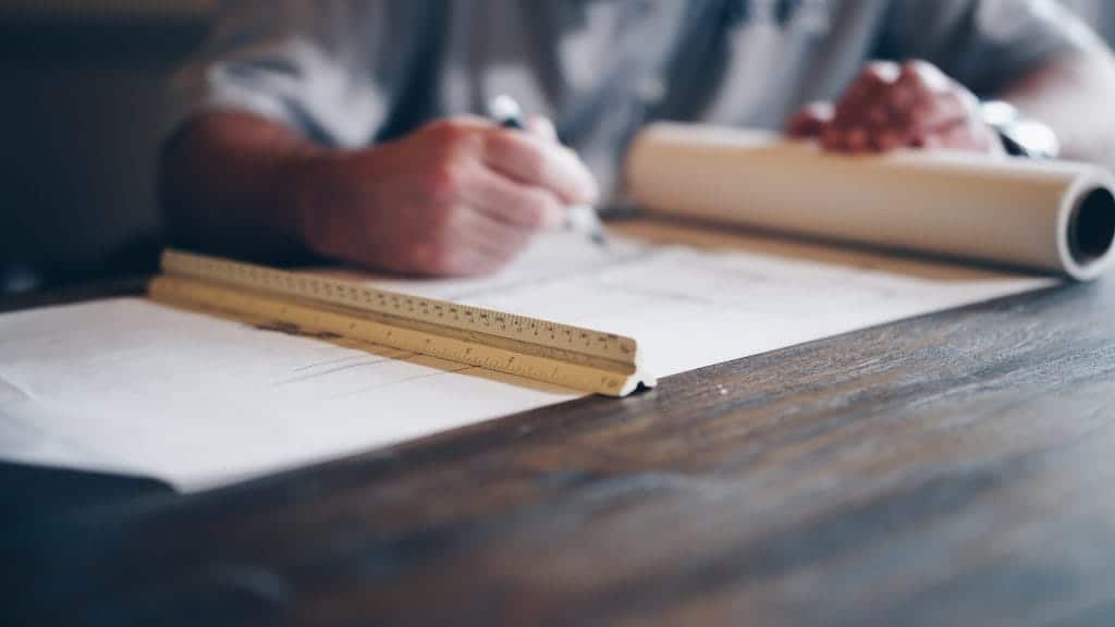 person writing on large sheet of paper and ruler