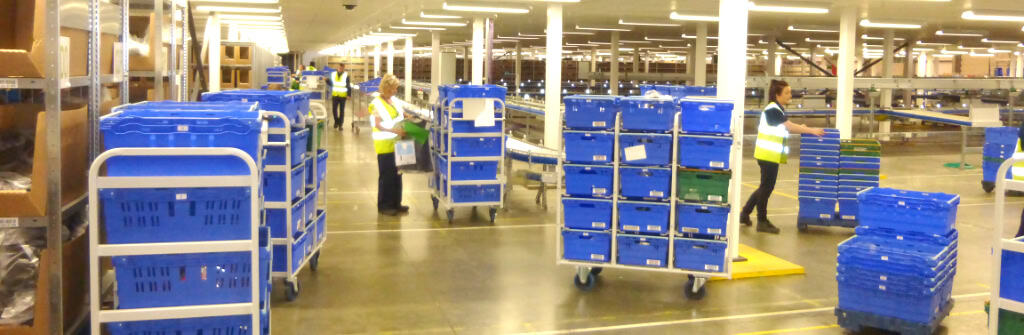 people working in warehouse with trolleys of tote boxes