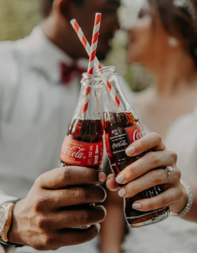 two people toasting with two bottles of coca cola